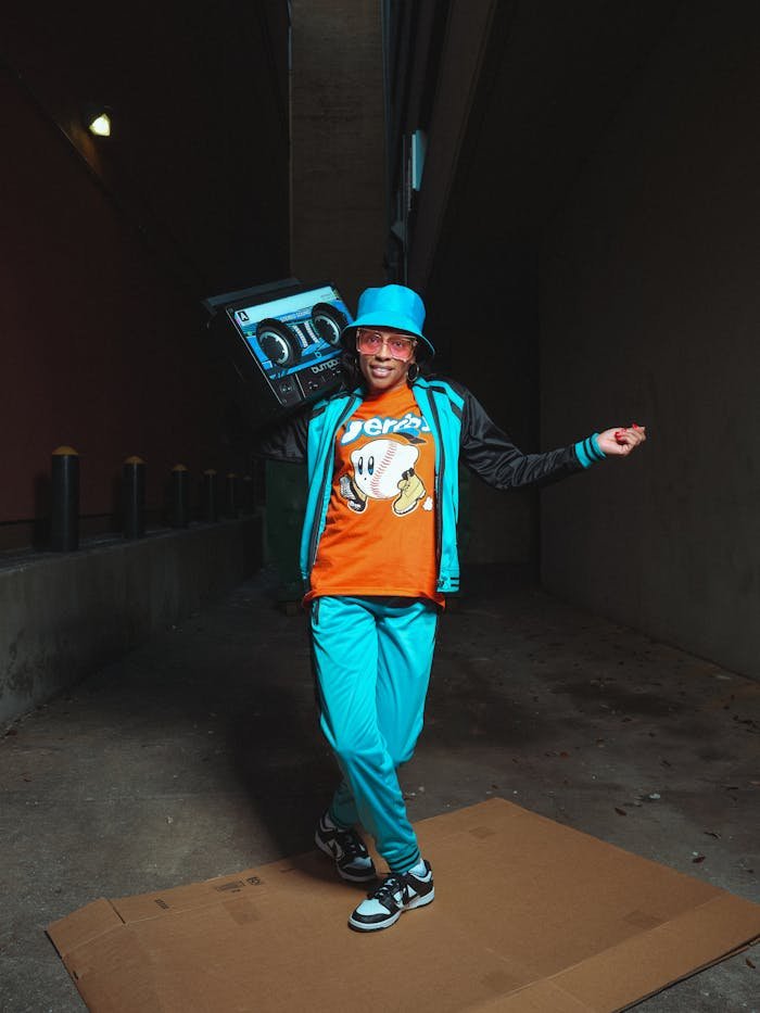 A stylish young man dances with a boombox in a dimly lit urban alley, showcasing 80s retro fashion.